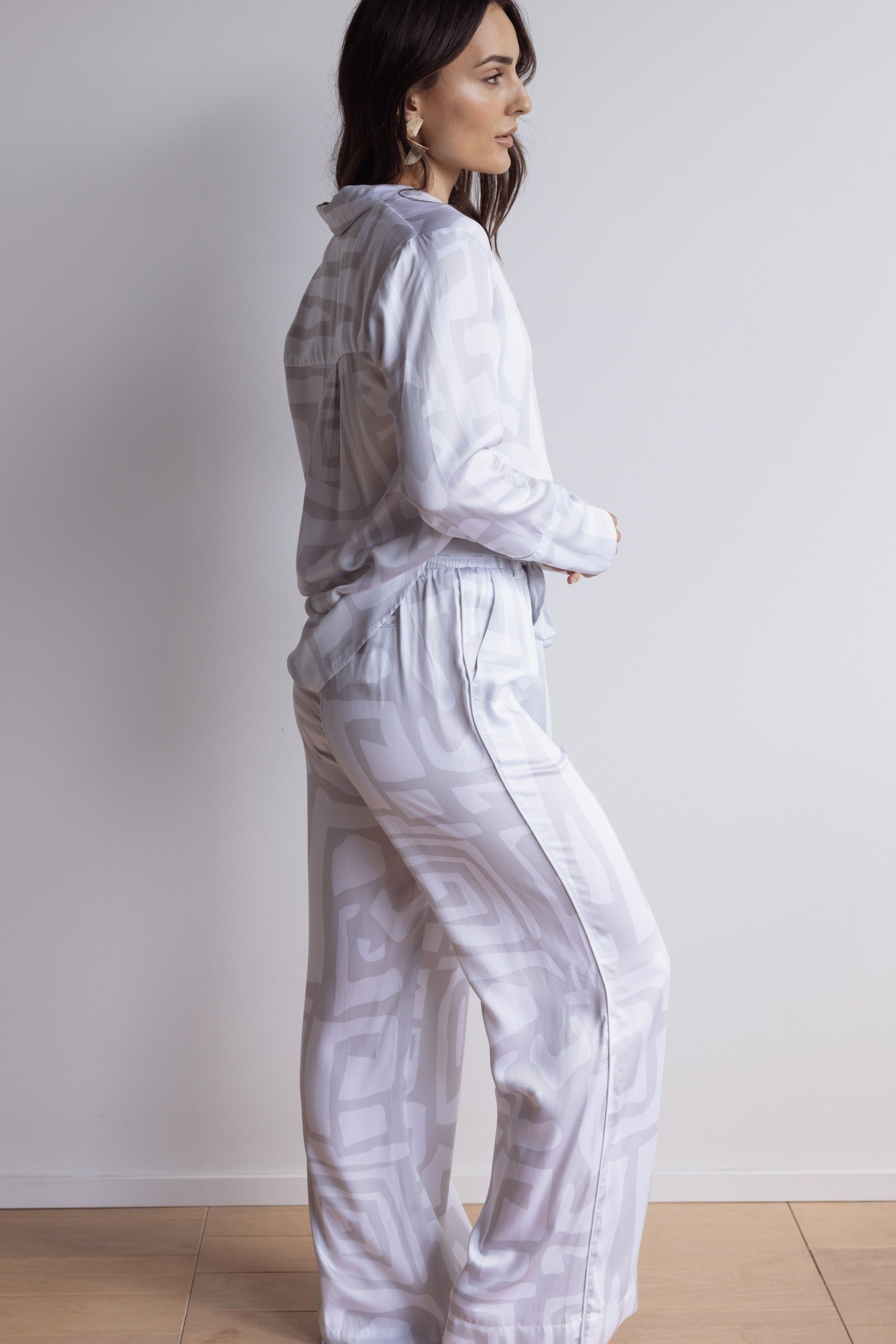 Woman standing in profile wearing a long-sleeve bamboo PJ top and pants with a soft white and grey bold geometric print