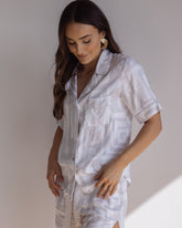 Woman wearing comfortable 100% bamboo PJ set showing a short sleeve pyjama top with button up design, pocket and bold geometric print in light grey and white.