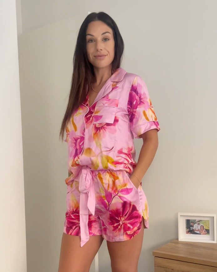 Customer wearing women's pink floral pyjama set with pockets, elegant piping, shell buttons and waist tie. Made from silky soft bamboo satin.