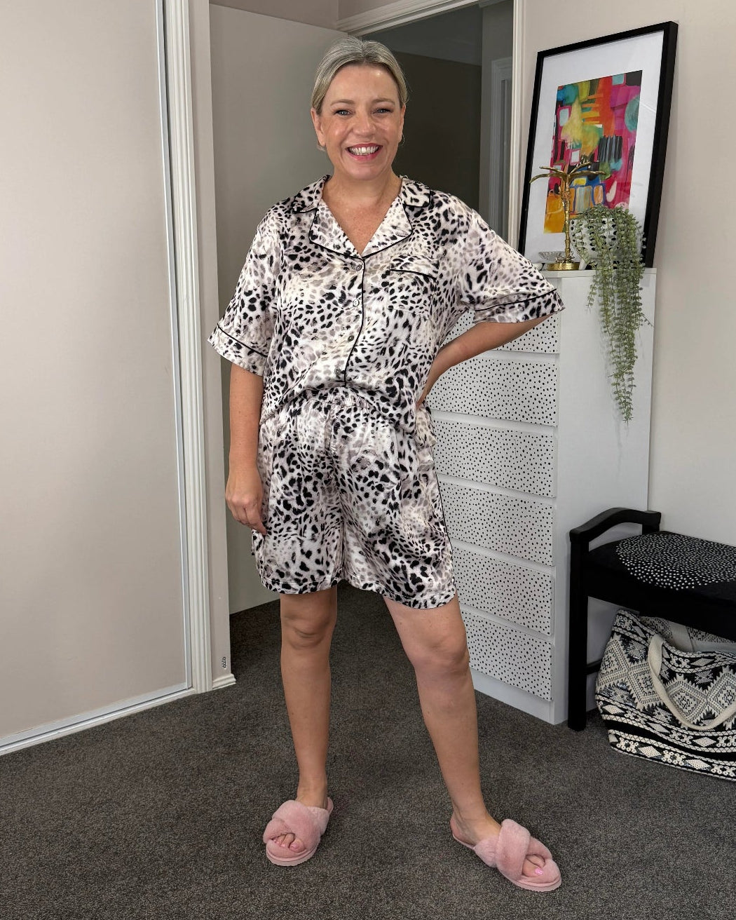 Woman wearing a silky bamboo short pyjama set with a soft animal print, featuring a relaxed button-up shirt and elastic-waist shorts, styled for breathable, luxe comfort at home.