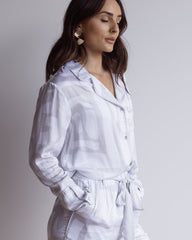 Woman wearing a white and grey long pyjama set. Made from silky soft bamboo satin. Long sleeve button up shirt, matching pants with pockets.