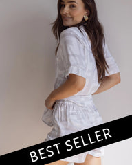 A female model wearing a short sleeve button-down bamboo pyjama top and matching PJ shorts with a graphic pattern, in a standing pose with a 'BEST SELLER' text overlay.