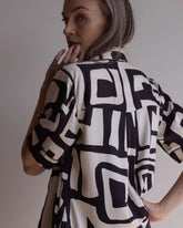 Woman looking over her shoulder wearing a short sleeve pyjama top and pants made of silky bamboo, with a bold geometric print in black and cream colour.