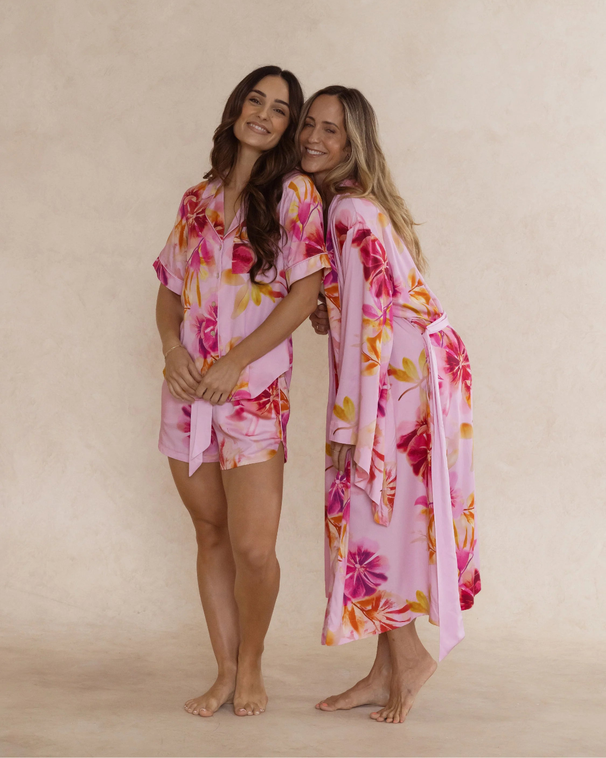 Two women wearing silky soft bamboo sleepwear in a pink floral print. One in kimono style robe, the other in a short pyjama set. Both items are sold as a sleepwear bundle for extra savings.