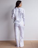 Woman wearing a long bamboo satin pyjama set in white and grey geometric pattern. With long sleeved shirt and pants.