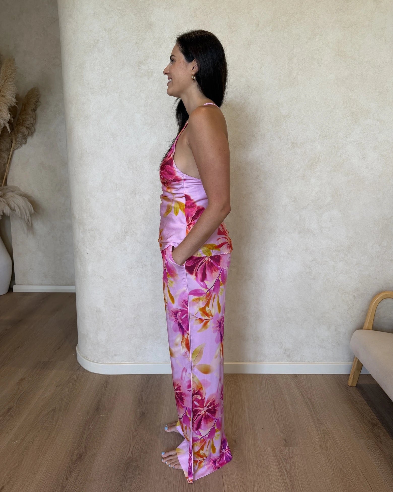 Side view of a woman wearing a pink floral pyjama set. Cami top with matching pants, including pockets.