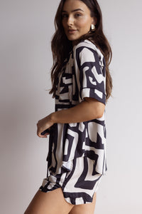 Woman wearing comfortable 100% bamboo PJ set showing a short sleeve pyjama top and shorts with a geometric print in black and cream.