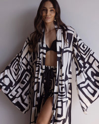 Woman wearing a kimono-style robe. Made from silky-soft bamboo satin with a flowing fit, featuring a unique print design and a tie waist for an adjustable fit. Hidden pockets and wide sleeves for a beautiful yet dramatic design. Perfect for lounging.