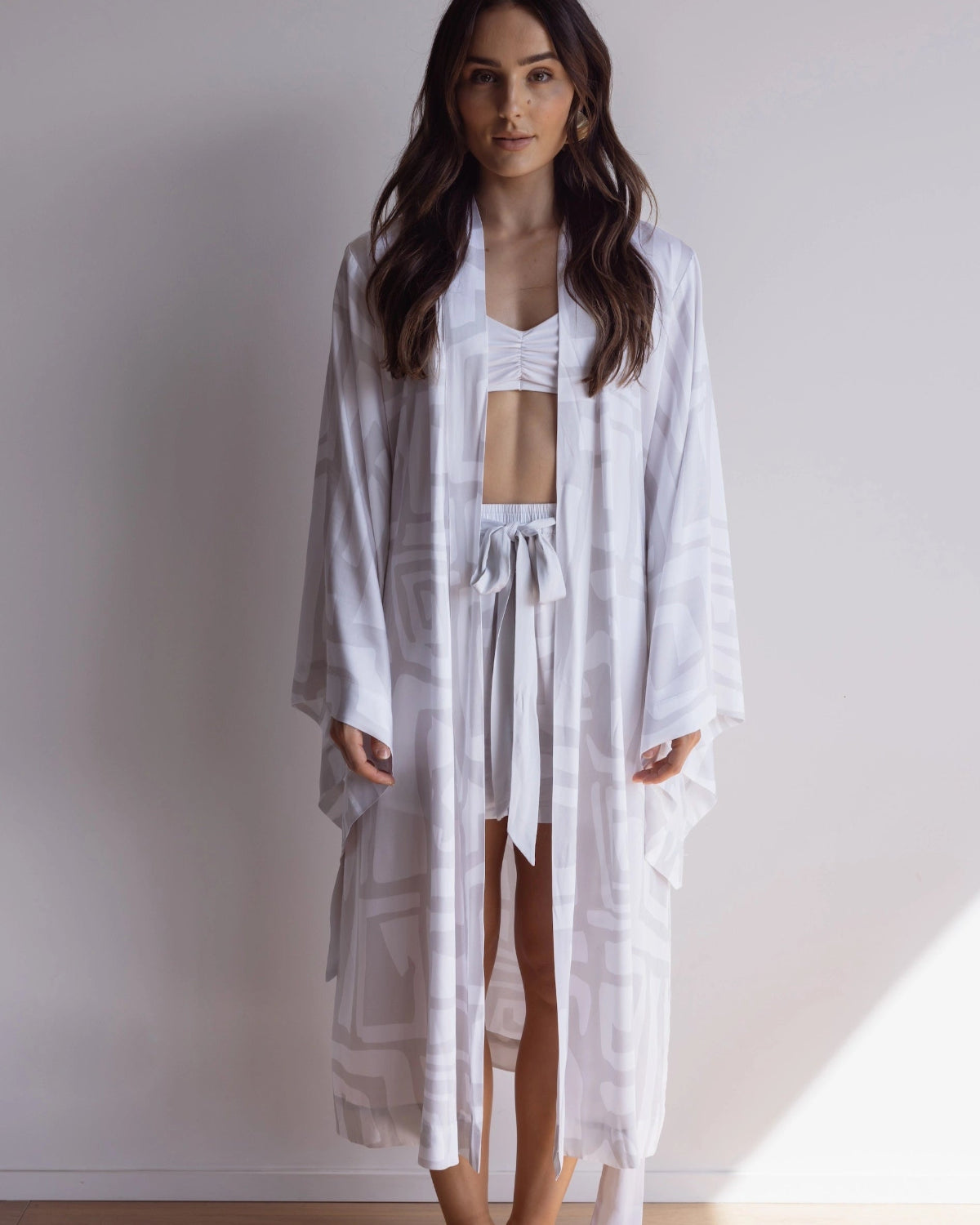 Woman wearing a comfortable kimono-style robe. Made from silky-soft, breathable bamboo. Featuring a unique print design and a tie waist for an adjustable fit and hidden pockets. Perfect for relaxing.
