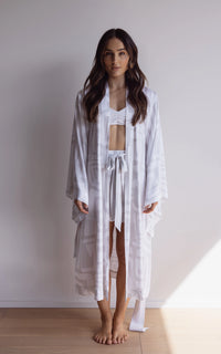 Woman wearing a comfortable kimono-style robe. Made from silky-soft, breathable bamboo. Featuring a unique print design and a tie waist for an adjustable fit and hidden pockets. Perfect for relaxing.