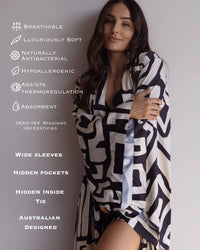 Woman hugging herself in a beautiful silky soft kimono-style robe, with wide sleeves, hidden pockets and hidden inside tie. Text on the image highlights the benefits of bamboo satin; breathable, luxuriously soft, naturally antibacterial, assists thermoregulation, absorbent.