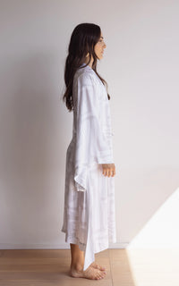 Woman wearing a comfortable kimono-style robe with wide sleeves. Made from silky-soft, breathable bamboo. Featuring a unique print design in light grey and white, with and a tie waist for an adjustable fit and hidden pockets. Perfect for relaxing.