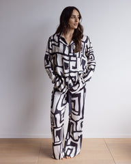 Woman wearing silky, breathable 100% bamboo PJ set showing a long sleeve pyjama top with button up design, pants with pockets and bold geometric print in black and cream.