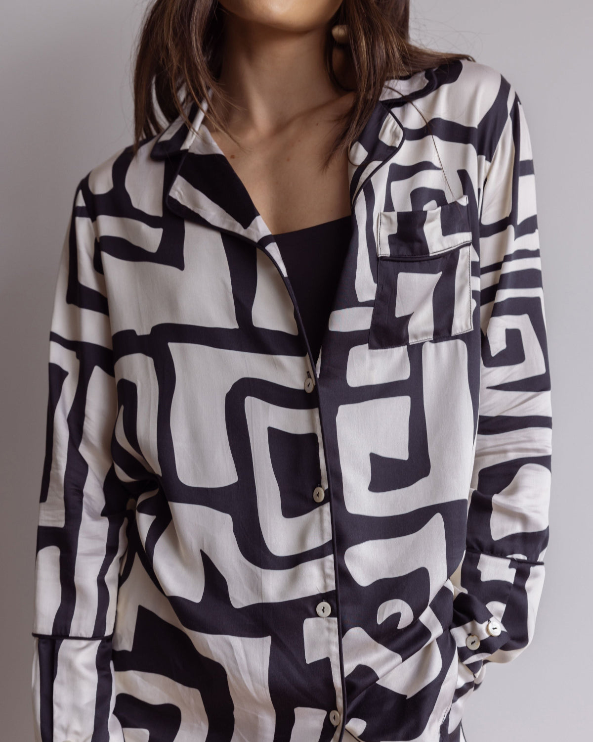 Woman wearing comfortable, breathable 100% bamboo PJ set showing a long sleeve pyjama top with button up design, pocket and bold geometric print in black and cream.