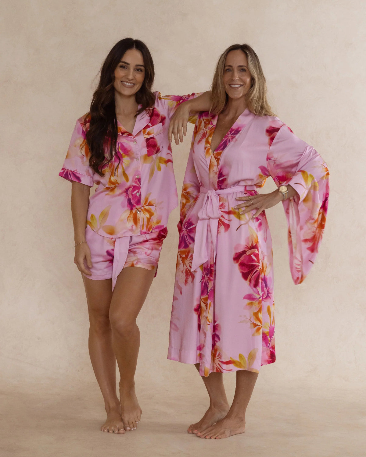Two women wearing silky soft bamboo sleepwear in a pink floral print. One in kimono style robe, the other in a short pyjama set. Both items are sold as a sleepwear bundle for extra savings.