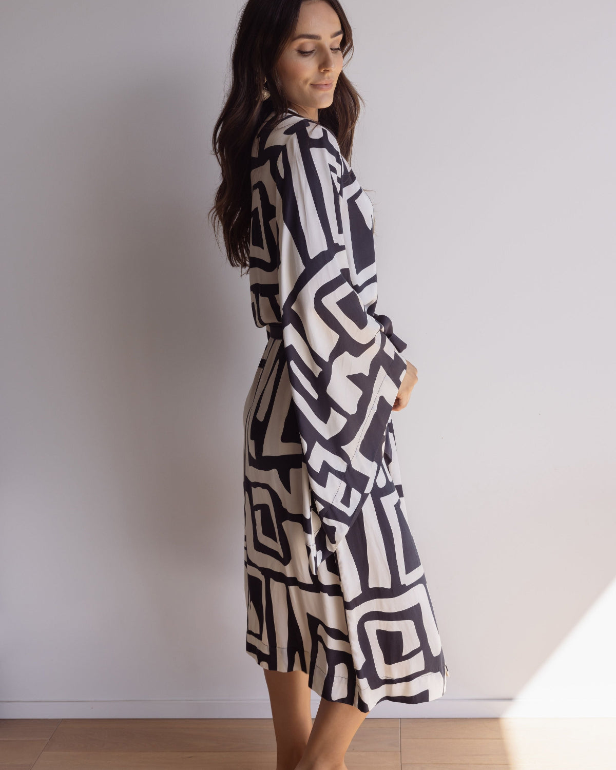 Woman wearing a kimono-style robe. Made from silky-soft, breathable bamboo with a flowing fit, featuring a unique print design in black and cream.  Beautiful design with a tie waist for an adjustable fit, pockets and wide sleeves. Perfect for lounging.
