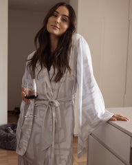 Woman wearing a comfortable kimono-style robe, made from silky-soft, breathable bamboo with a flowing fit, featuring a unique print design in grey and white. Tie waist for an adjustable fit and hidden pockets. Perfect for relaxing.