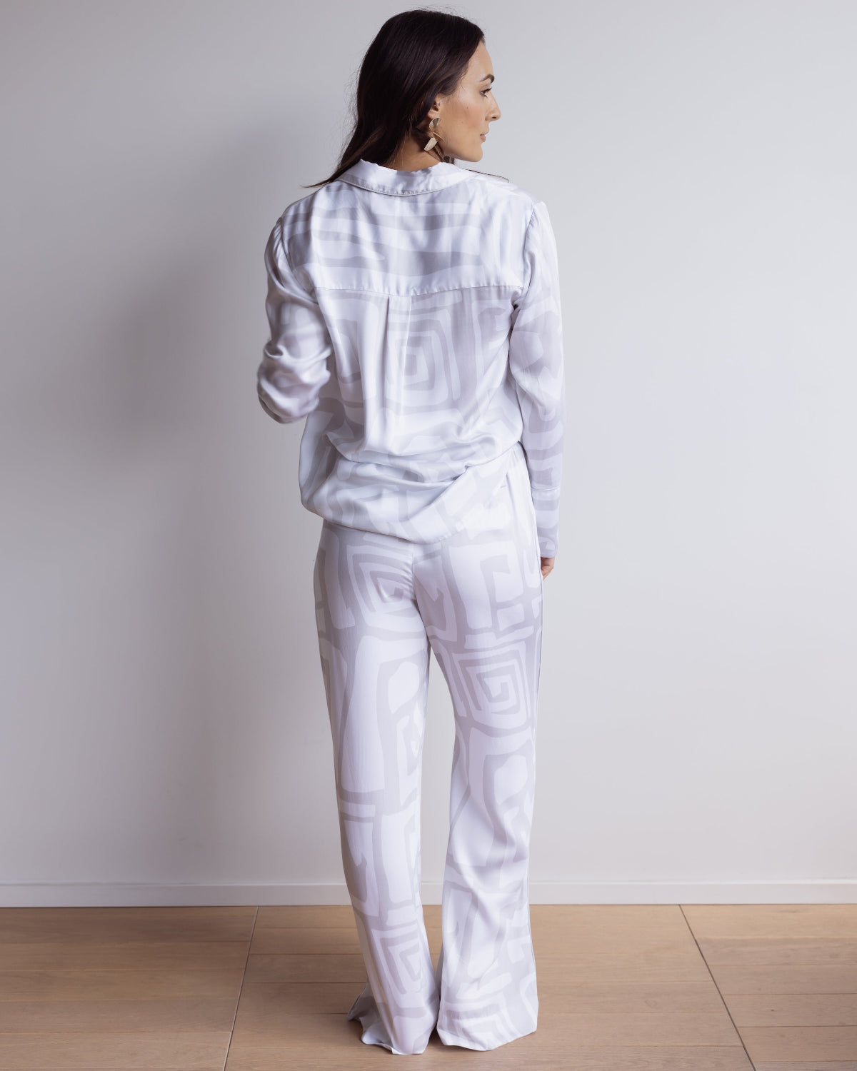 Woman wearing a long bamboo satin pyjama set in white and grey geometric pattern. With long sleeved shirt and pants.