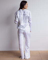 Woman wearing a long bamboo satin pyjama set in white and grey geometric pattern. With long sleeved shirt and pants.