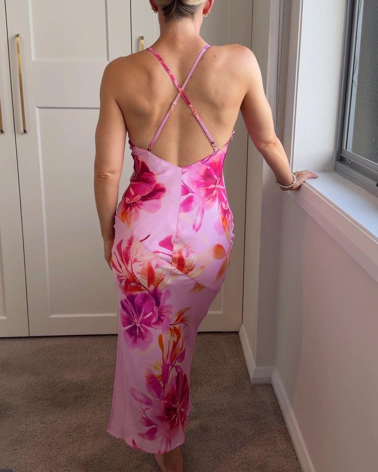 Back of a woman wearing a pink floral slip dress with cross over spaghetti straps and a low back.