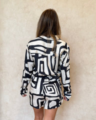 Back of a woman wearing a black and white geometric patterned pyjama set. With long sleeve button up shirt, and matching shorts.