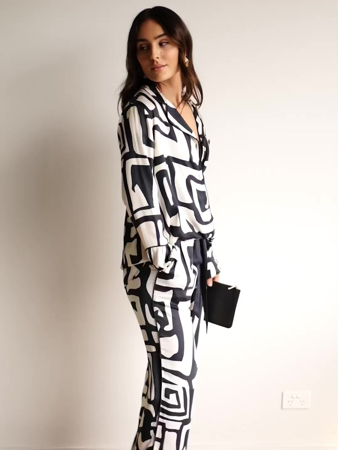 Video of a woman in a long pyjama set, made from satin bamboo, with a bold print, showing the fit in both black & cream colour and grey & white.