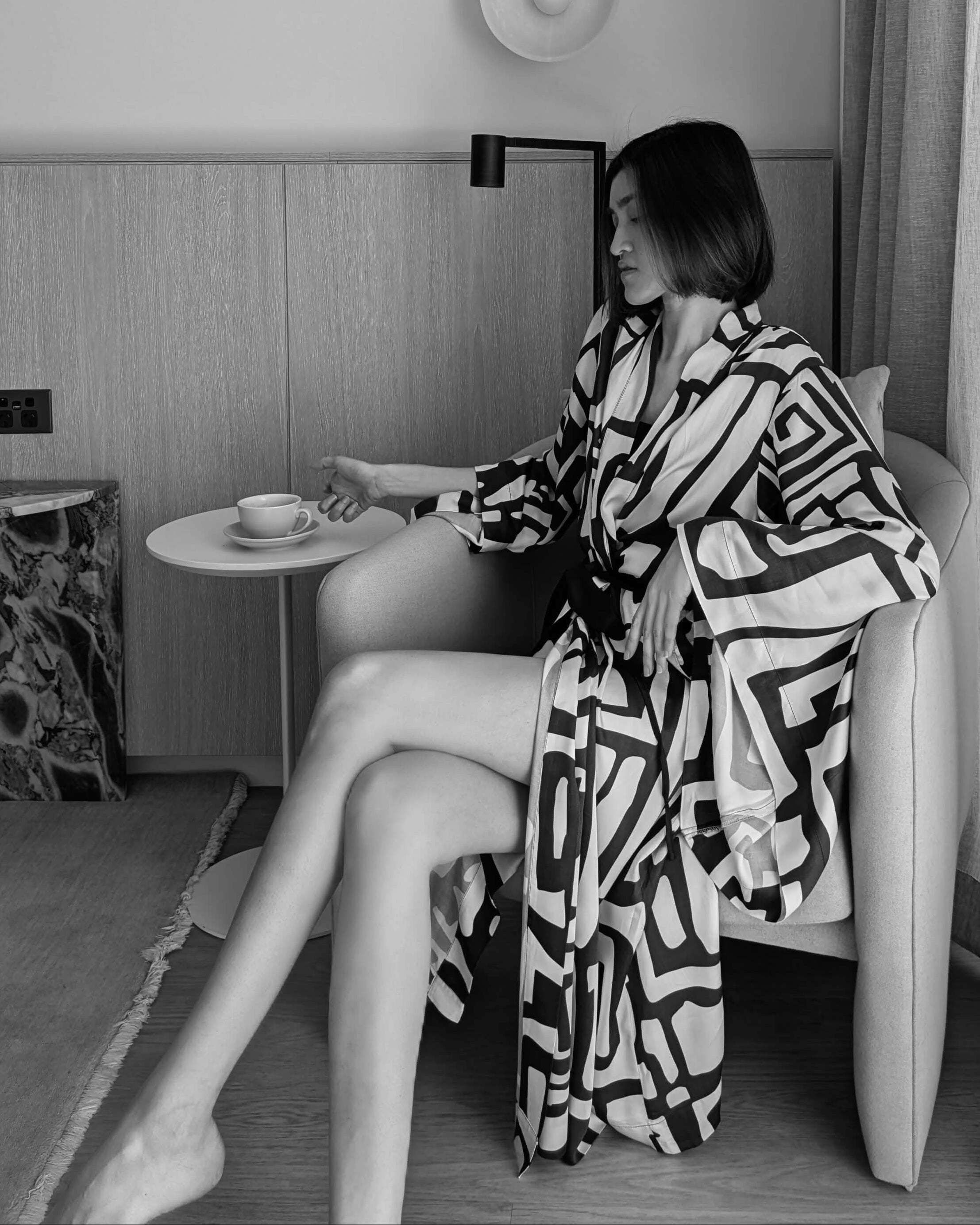 Woman sitting in wearing a black and cream kimono-style robe. With wide sleeves, made from silky bamboo satin.