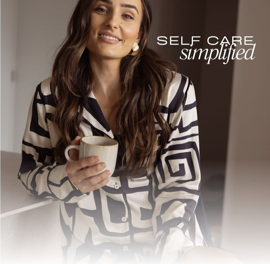 Woman smiling in silky bamboo pyjamas holding a mug with 'Self Care Simplified' text in the background